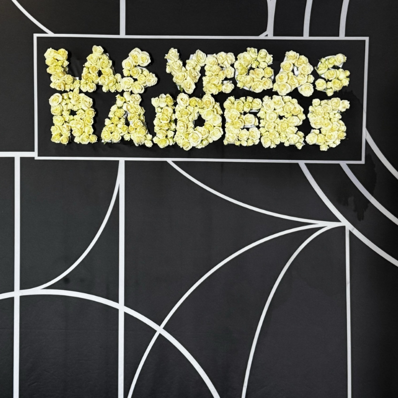 Custom Las Vegas Raiders sign spelled out with fresh white roses on a black geometric backdrop.