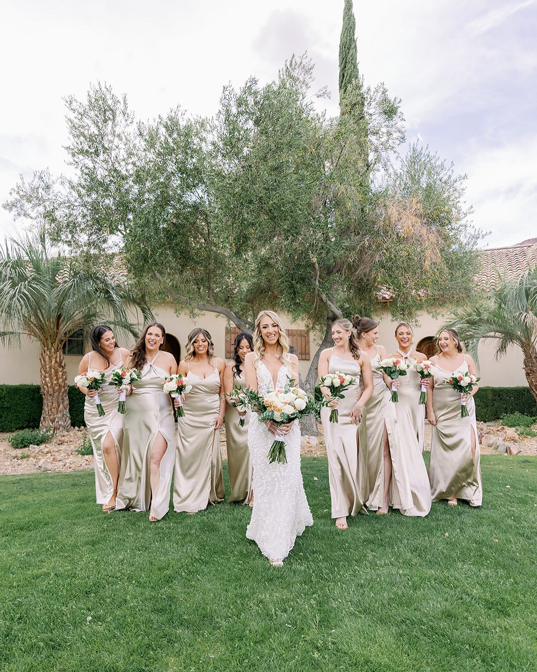 Bride with eight bridesmaids in champagne satin dresses holding wedding bouquets on a lawn in Las Vegas