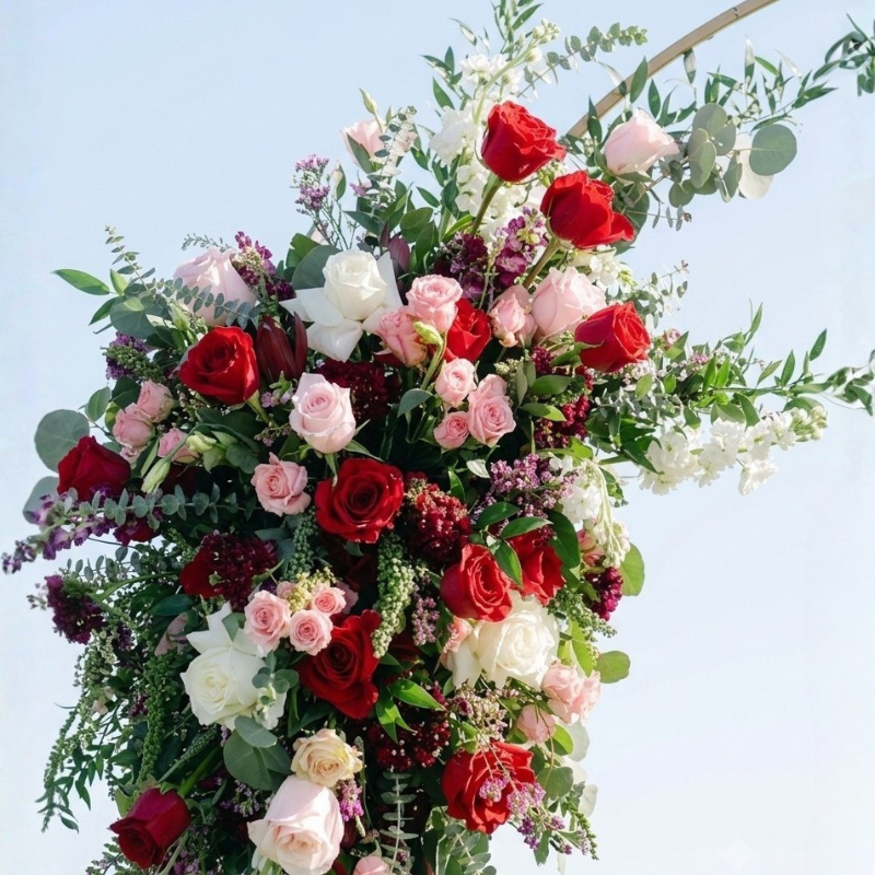 Close-up of a vibrant wedding arch
arrangement featuring red roses, pink garden roses, and white stock flowers.