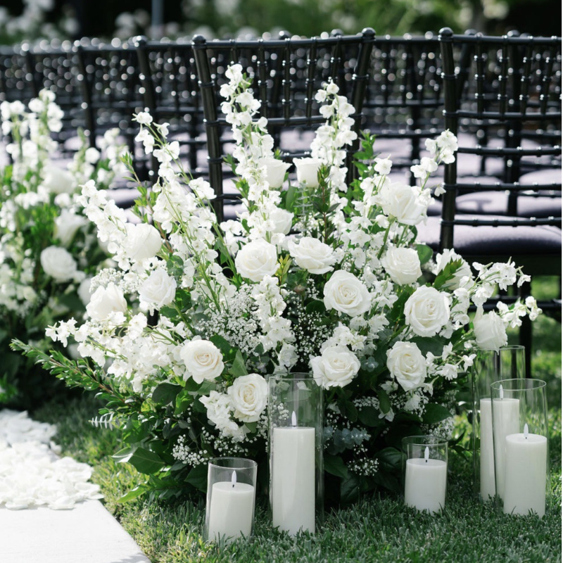 White rose and delphinium wedding ceremony aisle flowers with pillar candles in glass
cylinders.