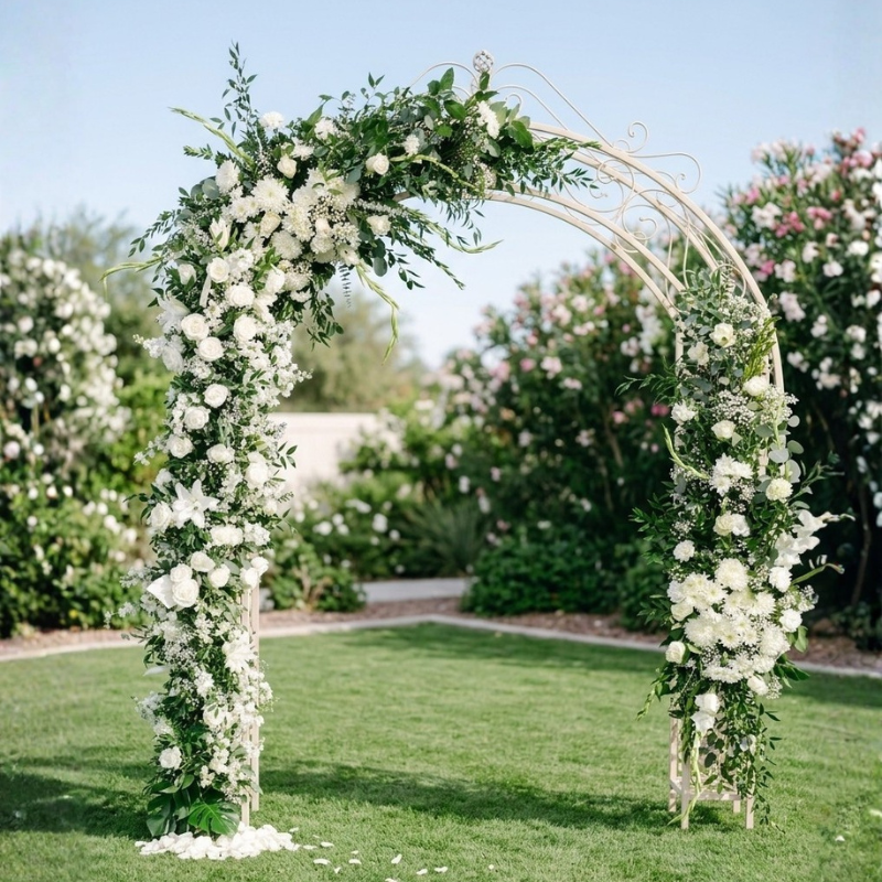 White wedding arch decorated with fresh white roses and lush greenery for a garden ceremony backdrop.