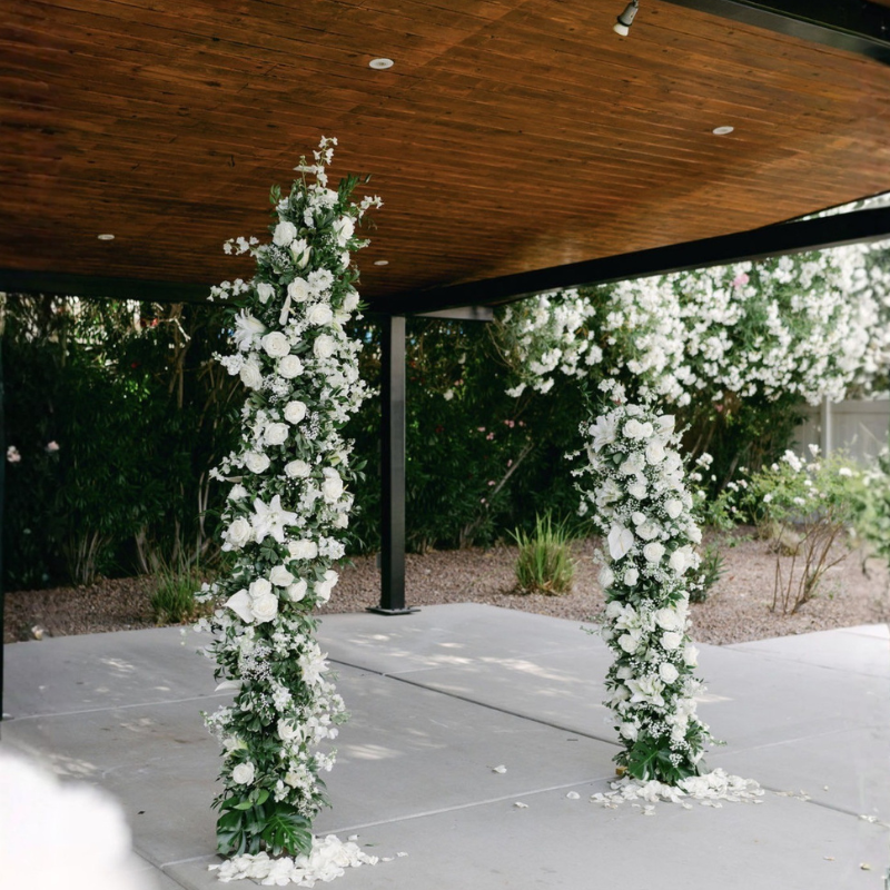 Elegant white floral pillars with lush greenery for an outdoor wedding ceremony backdrop.