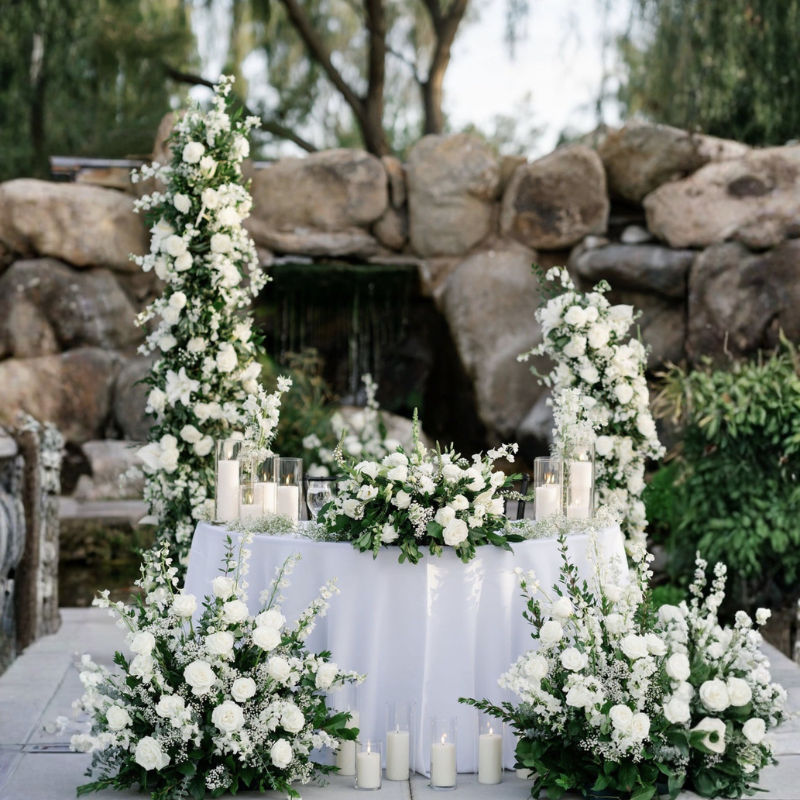 White rose sweetheart table centerpiece arrangement framed by floral pillars and romantic candles.
