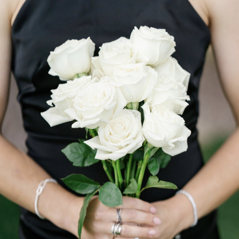Bridesmaid in black dress holding a classic hand-tied bouquet of fresh white roses.